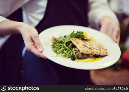 Chef hands holding fried Salmon fish fillet with vegetables for dinner in a restaurant kitchen. Chef hands holding dish of fried Salmon fish fillet