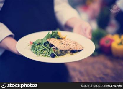 Chef hands holding fried Salmon fish fillet with vegetables for dinner in a restaurant kitchen. Chef hands holding dish of fried Salmon fish fillet