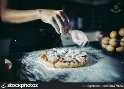 Chef hands pouring flour powder on raw dough. Cooking concept.