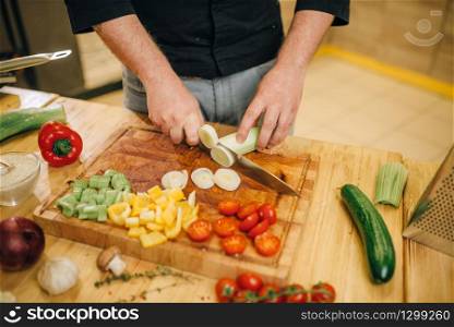 Chef hands with knife cuts mushrooms on wooden board closeup. Man cutting vegetables on counter, fresh salad cooking, kitchen interior on background. Male person chopping ingredients for lettuce. Chef with knife cuts mushrooms on wooden board