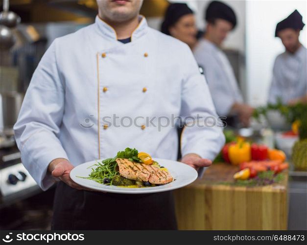Chef holding fried Salmon fish fillet with vegetables for dinner in a restaurant kitchen. Chef holding dish of fried Salmon fish fillet