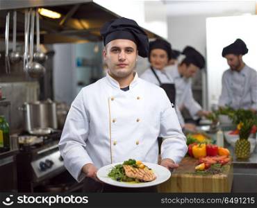 Chef holding fried Salmon fish fillet with vegetables for dinner in a restaurant kitchen. Chef holding dish of fried Salmon fish fillet