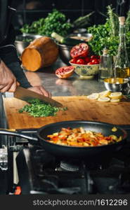 Chef holding knife, cutting parsley on wooden cutting board in vegan restaurant. Chef Holding a Knife and Cutting Parsley on a Wooden Cutting Board