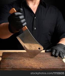 chef in a black shirt and black latex gloves holds a large kitchen knife for cutting meat, low key