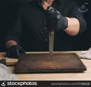 chef in a black shirt and black latex gloves holds a large kitchen knife for cutting meat, low key
