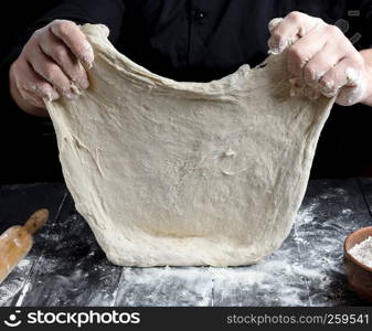 Chef in black jacket, kneads dough from white wheat flour, close up