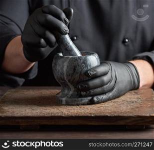 Chef in black latex gloves holds a stone mortar with a mixture of peppers, cooking and grinding spices