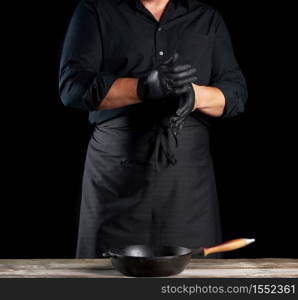 chef in black shirt and apron puts black latex gloves on his hands before preparing food, black background