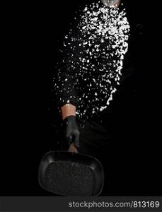 Chef in black uniform holds a pan with white salt and throws up, selective focus, blurred grains of seasoning