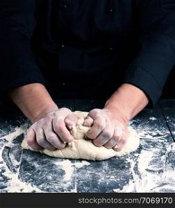 chef in black uniform kneads white wheat flour dough on the table