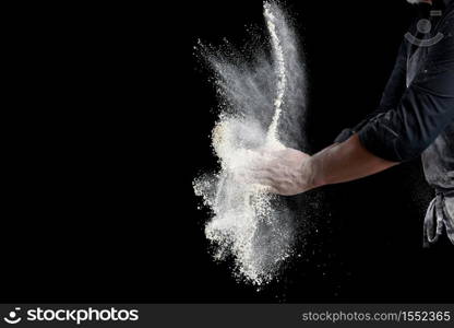chef in black uniform sprinkles white wheat flour in different directions, product scatters dust, black background, copy space