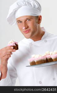 Chef in chef?s whites and toque holding and eating cupcakes