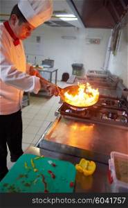 chef in hotel kitchen prepare vegetable food with fire