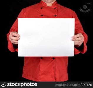 chef in red uniform holding a blank white paper sheet on a black background, copy space