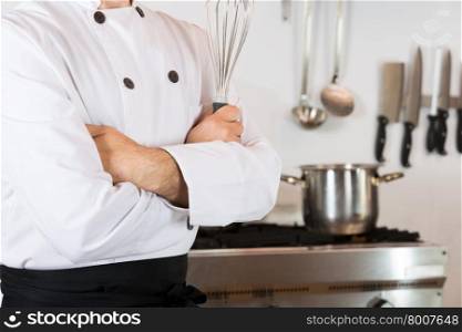 Chef in the kitchen with his arms crossed and with a whisk