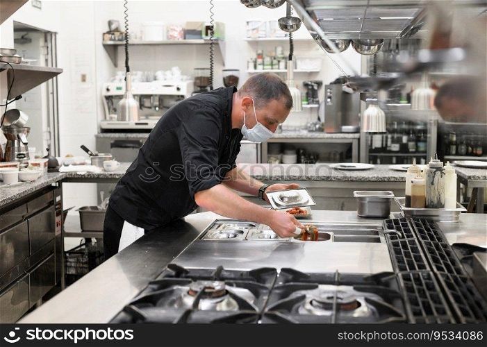 Chef in uniform cooking in a commercial kitchen. Male cook wearing apron standing by kitchen counter preparing food. High quality photo. Chef in uniform cooking in a commercial kitchen. Male cook wearing apron standing by kitchen counter preparing food.