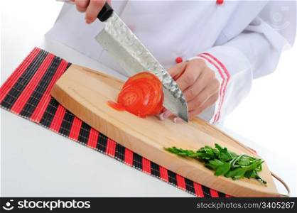 Chef in uniform cuts the tomato in the kitchen. Isolated on white background