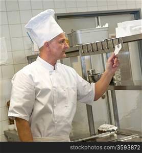 Chef in uniform reading orders in restaurant&acute;s kitchen