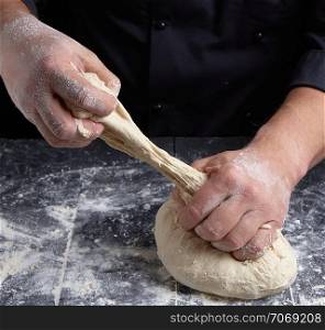 chef kneads dough made of white wheat flour on a black wooden table