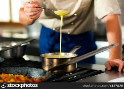 Chef - only torso to be seen - in a restaurant or hotel kitchen cooking; he is preparing the sauce