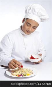 Chef placing cherry tomato on plate of noodles