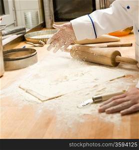 Chef pouring flour to dough and rolling pin wooden table