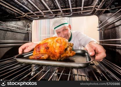 Chef prepares roast chicken (focus on chicken) in the oven, view from the inside of the oven. Cooking in the oven.