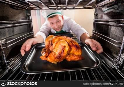 Chef prepares roast chicken (focus on chicken) in the oven, view from the inside of the oven. Cooking in the oven.