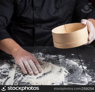Chef prepares the dough of white flour, in your hand round wooden sieve