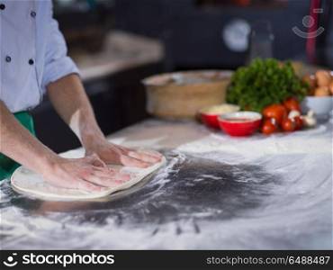 chef preparing dough for pizza rolling with hands on sprinkled with flour table. chef preparing dough for pizza