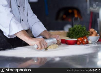 chef preparing dough for pizza rolling with rolling pin on sprinkled with flour table. chef preparing dough for pizza with rolling pin