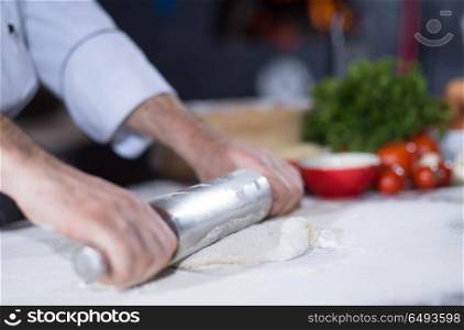 chef preparing dough for pizza rolling with rolling pin on sprinkled with flour table. chef preparing dough for pizza with rolling pin