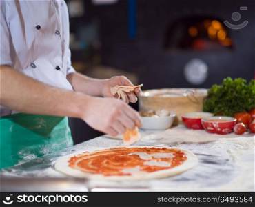 chef putting cut sausage or ham over pizza dough on kitchen table. chef putting cut sausage or ham on pizza dough