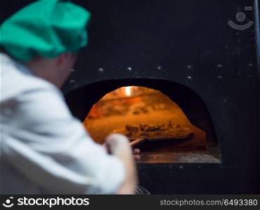 chef putting delicious pizza to brick wood oven with firewood and flame. chef putting delicious pizza to brick wood oven
