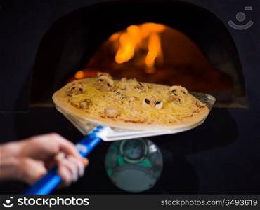 chef putting delicious pizza to brick wood oven with firewood and flame. chef putting delicious pizza to brick wood oven