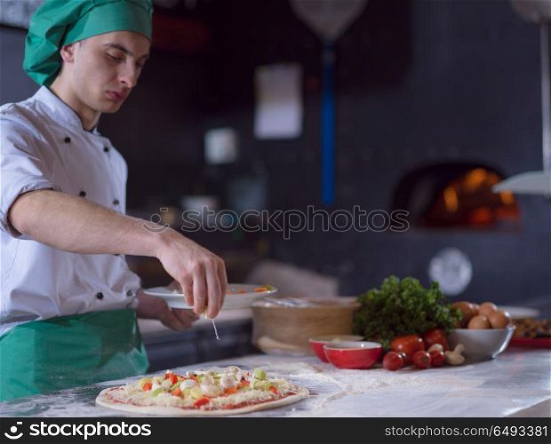chef putting fresh vegetables over pizza dough on kitchen table. chef putting fresh vegetables on pizza dough