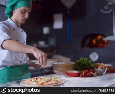 chef putting fresh vegetables over pizza dough on kitchen table. chef putting fresh vegetables on pizza dough