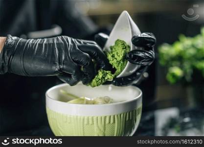 Chef’s hand in black gloves preparing pesto Genovese in vegetarian restaurant, close-up.. Chef’s Hand Preparing Pesto Genovese in Vegetarian Restaurant