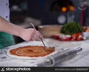 Chef smearing pizza dough with ketchup