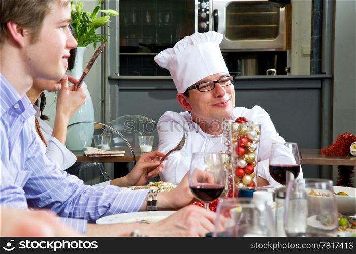Chef, socializing with his customers and dinner guests with the citchen in the background