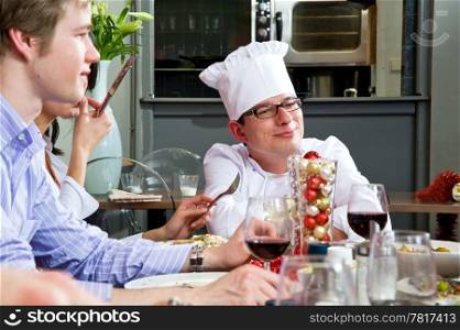Chef, socializing with his customers and dinner guests with the citchen in the background