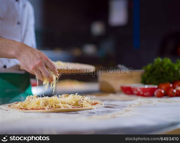 chef sprinkling cheese over fresh pizza dough on kitchen table. chef sprinkling cheese over fresh pizza dough