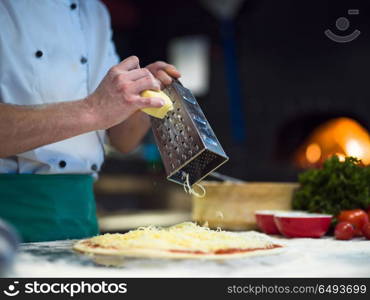 chef sprinkling cheese over fresh pizza dough on kitchen table. chef sprinkling cheese over fresh pizza dough