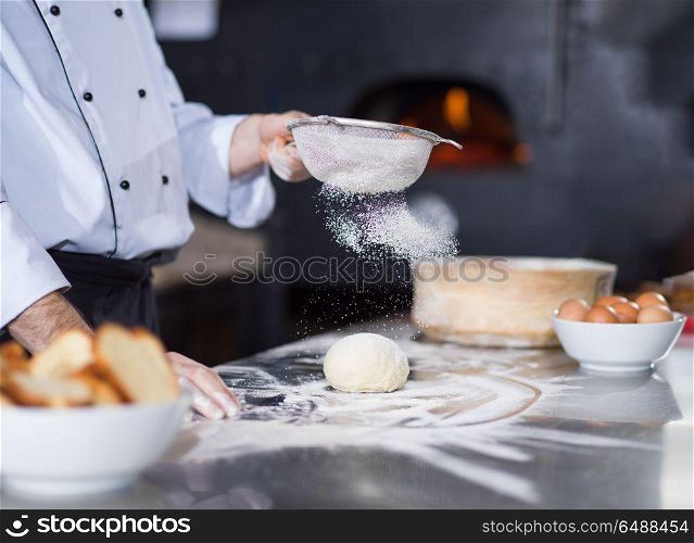 chef sprinkling flour over fresh pizza dough on kitchen table. chef sprinkling flour over fresh pizza dough