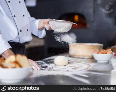 chef sprinkling flour over fresh pizza dough on kitchen table. chef sprinkling flour over fresh pizza dough