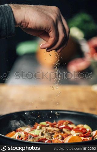 Chef sprinkling oregano over vegetables in a pan, motion blur . Seasoning - Chef Sprinkling Oregano over Vegetables 