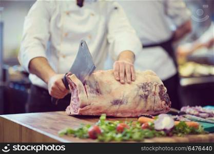 chef using ax while cutting big piece of beef on wooden board in restaurant kitchen. chef cutting big piece of beef