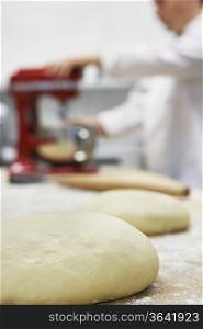 Chef using dough mixer in kitchen, focus on dough in foreground