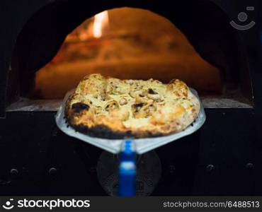 chef using special shovel to removing hot pizza from stove where it was baked. chef removing hot pizza from stove