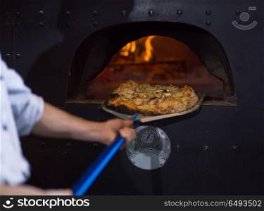 chef using special shovel to removing hot pizza from stove where it was baked. chef removing hot pizza from stove